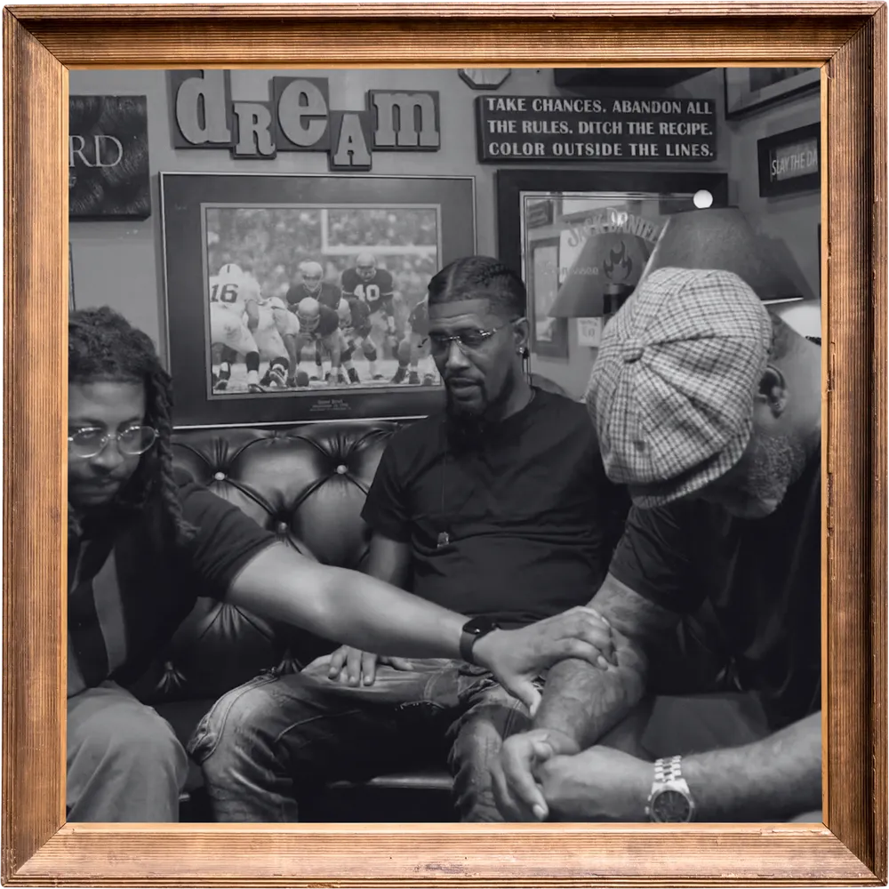 Black-and-white photo in a wooden frame of men sitting close together on a barbershop couch